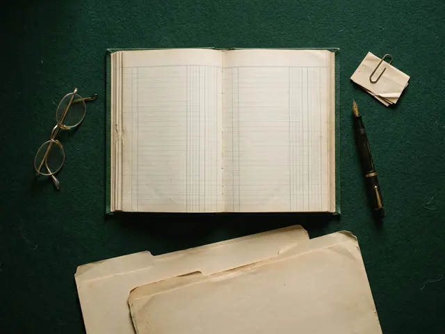An open accounting ledger, fountain pen and manila folders arranged on a dark green surface